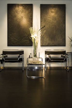 A reception area with two black benches, a glass table with a vase of flowers, and two large abstract paintings on the wall. - Aussen Alster Hotel (Hamburg)