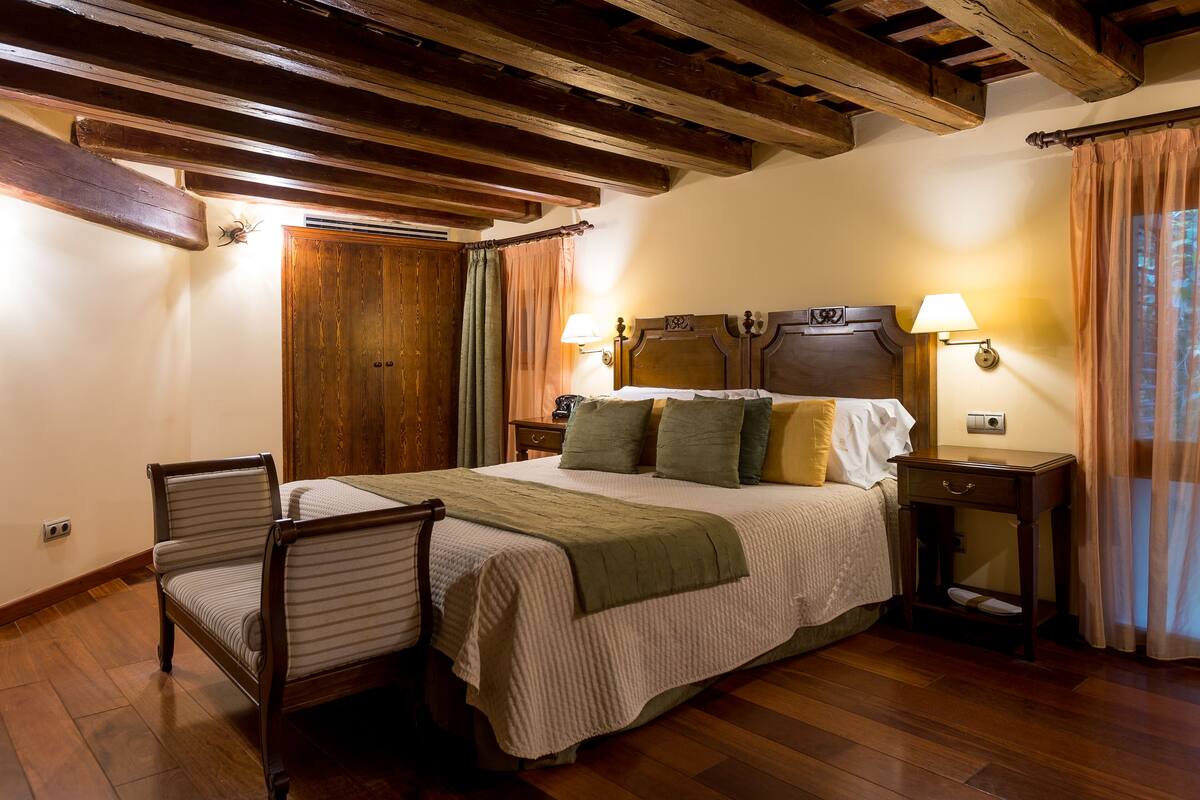 Un dormitorio con una cama de madera, dos lámparas de noche, una silla y un armario de madera.