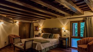 A cozy bedroom with a wooden ceiling, a large bed, two bedside tables with lamps, a chair, and a window with curtains. - Hotel Villa Retiro (Xerta)
