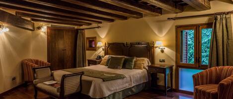 A cozy bedroom with a wooden ceiling, a large bed, two bedside tables with lamps, a chair, and a window with curtains.