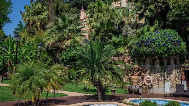 A swimming pool surrounded by lush greenery and a castle-like structure. - Hotel Villa Retiro (Xerta)