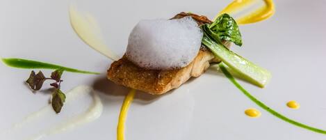 Un plato con un elemento esférico encima, adornado con hojas verdes y salsa amarilla.
