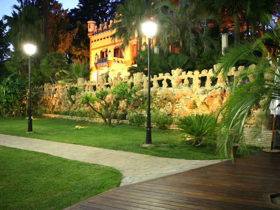 Un jardín bien iluminado con muro de piedra, sendero y palmeras.