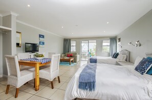 A hotel room with a large bed, a dining table with chairs, a TV, and a balcony with a view. - Cape St Francis Resort (Cape Saint Francis)
