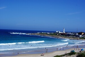 A beach with waves, people, and a lighthouse.