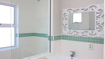 A bathroom with a glass shower enclosure, a white sink, and a decorative mirror with a green-tiled backsplash.