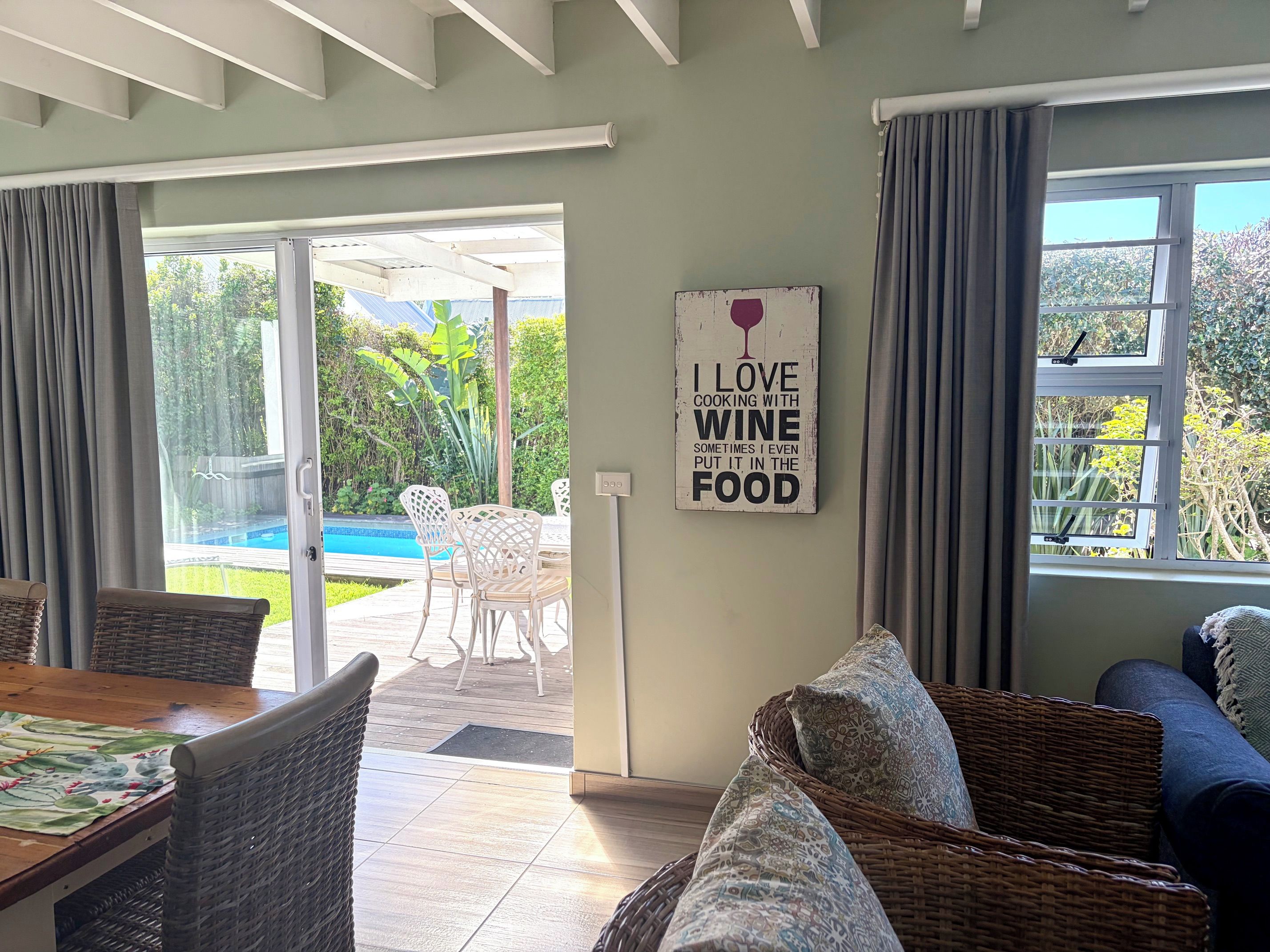 Una habitación con comedor, sofá, una pared con letrero relacionado con el vino, y vista a una piscina y follaje exterior.
