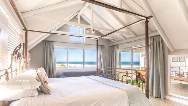 Ruime slaapkamer met een hemelbed, grote ramen en een balkon met uitzicht op de oceaan.