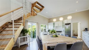 Een moderne keuken met witte kasten, een houten trap en een eetgedeelte met een grote tafel en stoelen.