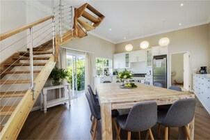 A modern kitchen with white cabinets, a wooden staircase, and a dining area with a large table and chairs.