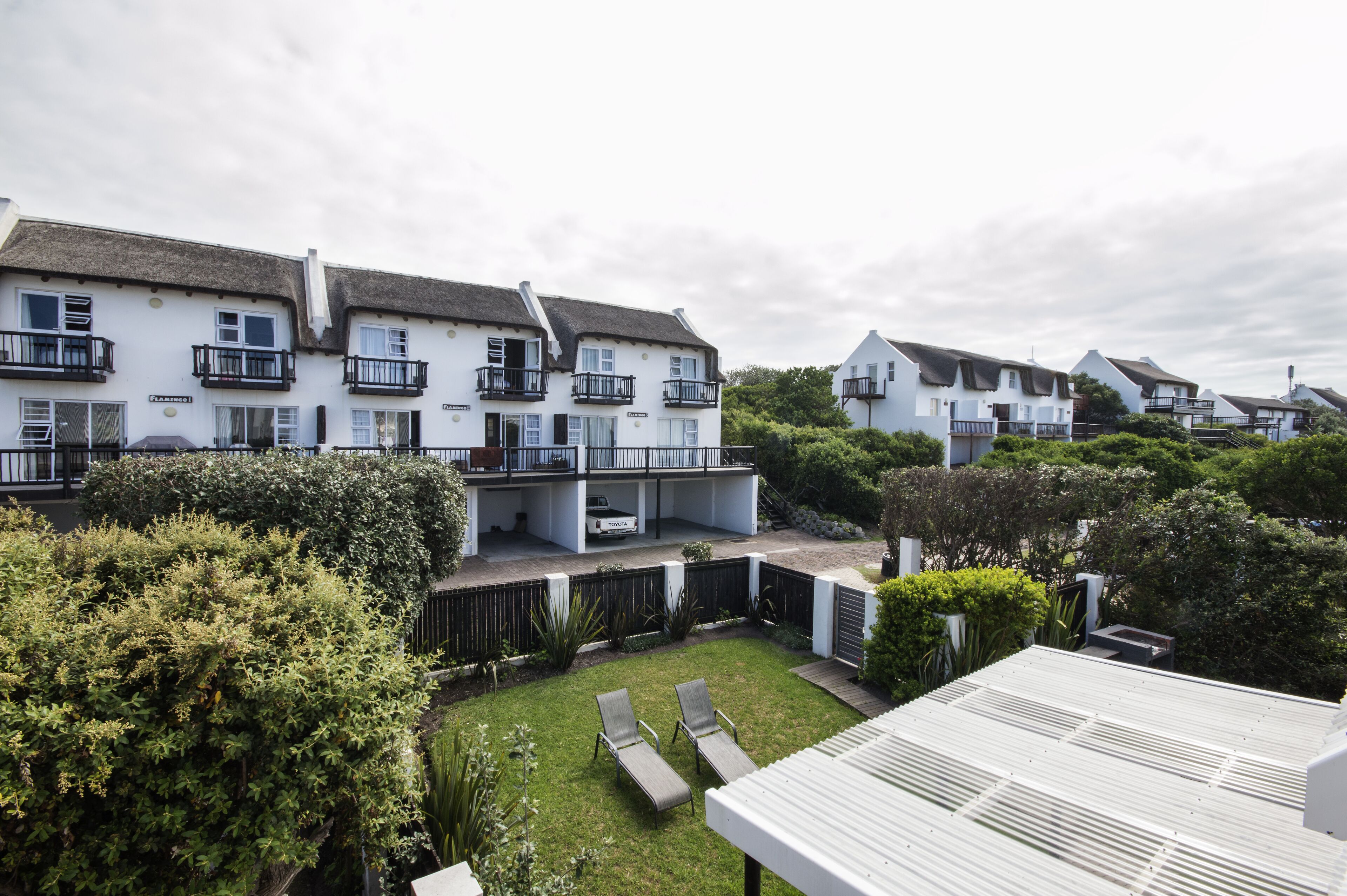 A residential building with multiple balconies, a well-maintained lawn, and a white fence.