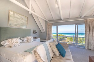 A bedroom with a large bed, a sofa, and a balcony with a view of the ocean.