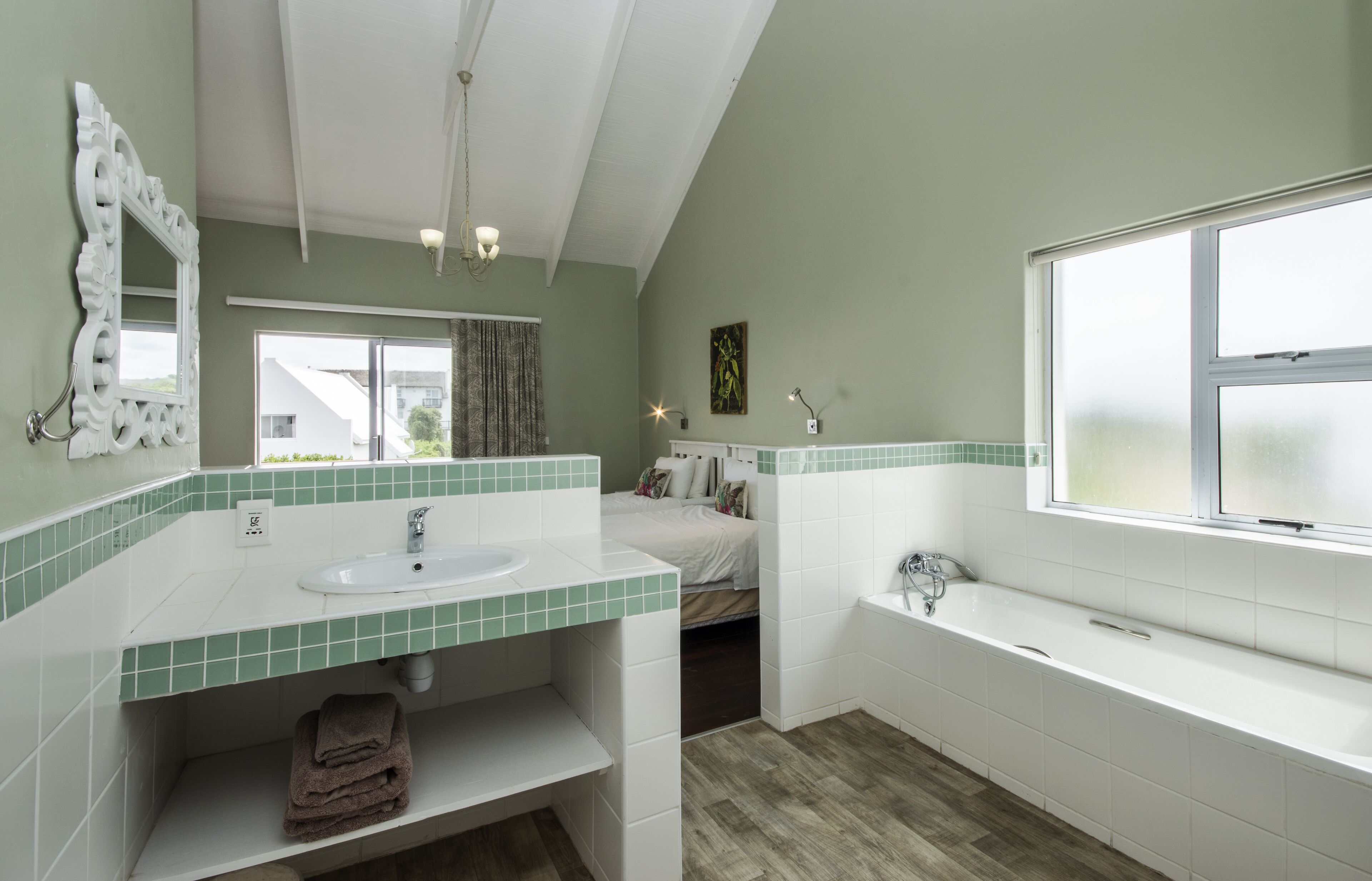 Un baño moderno con un ventanal grande, un lavamanos blanco, una bañera y un espejo.