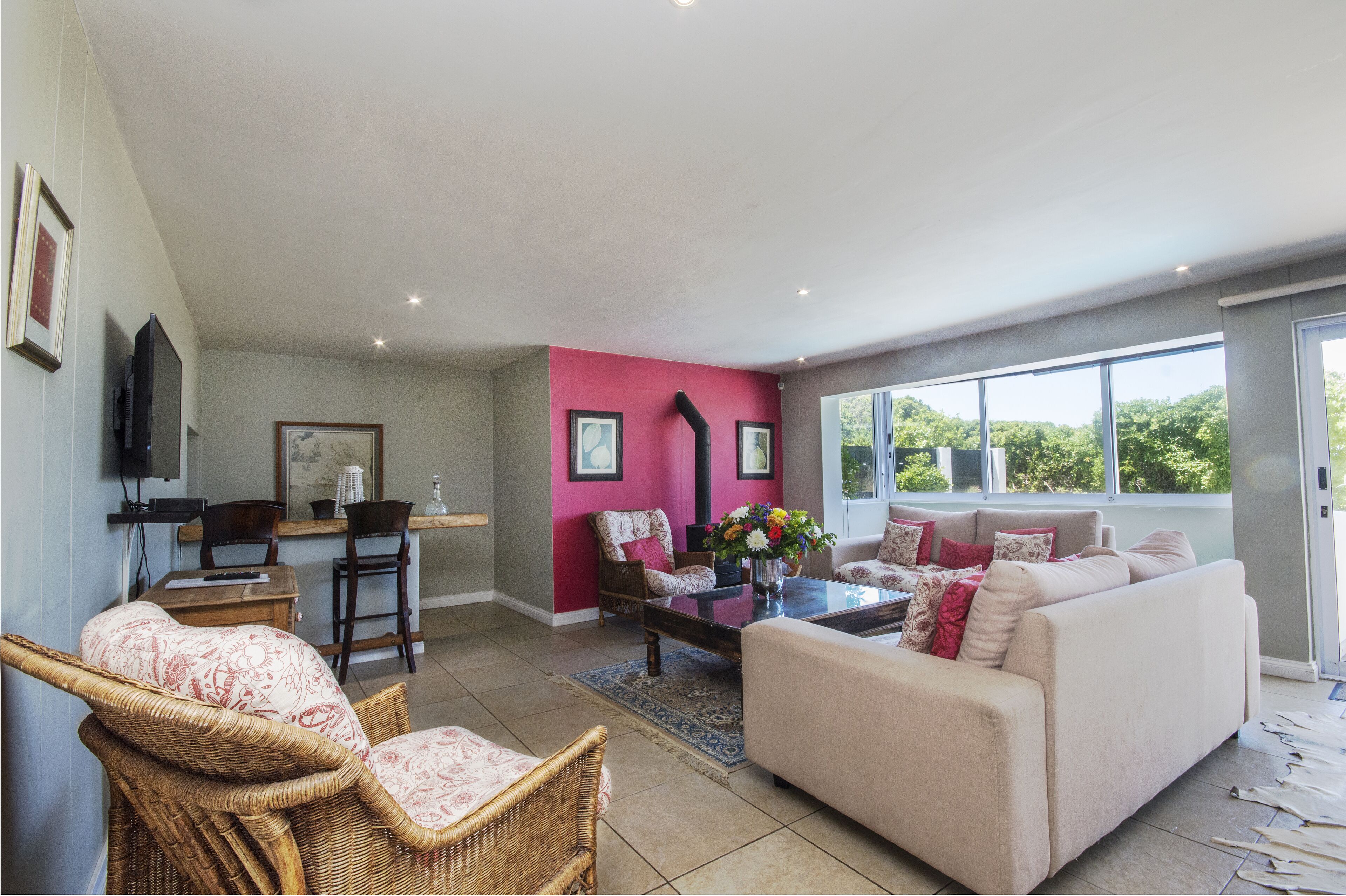 A spacious living room with a beige sofa, wicker chairs, a coffee table, and a pink accent wall.