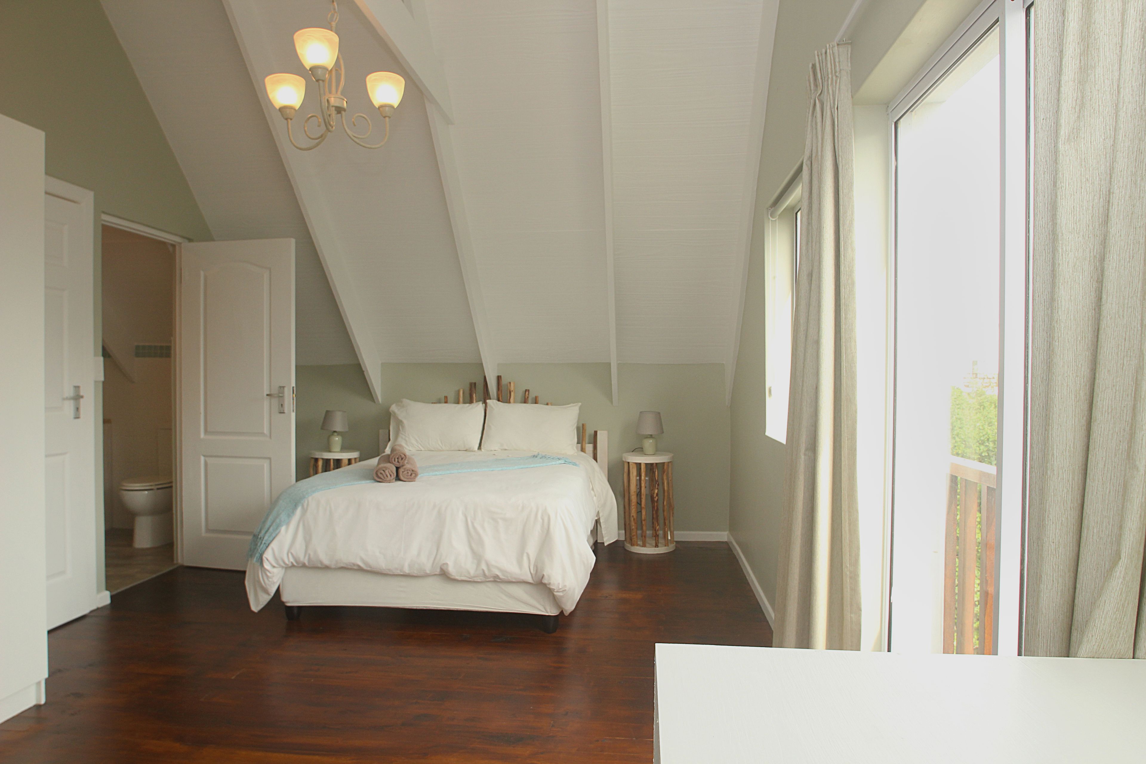 A bedroom with a large bed, a chandelier, a window with curtains, and a door leading to another room.