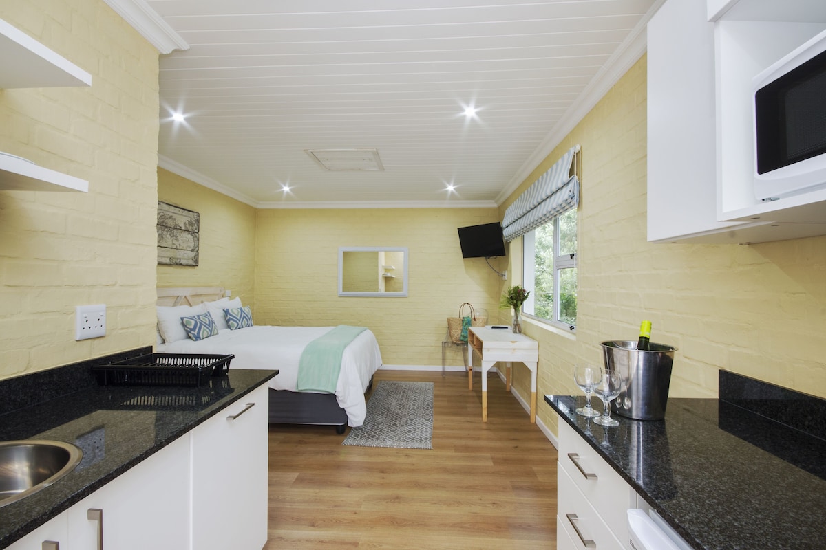 A compact hotel room with a bed, kitchenette, and a small dining area.