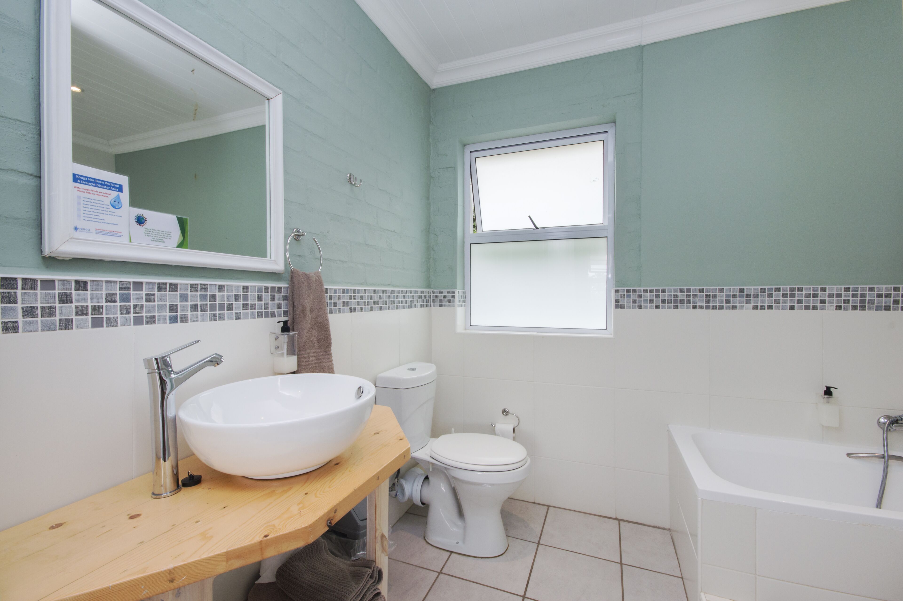 A bathroom with a white sink, toilet, and bathtub, a wooden vanity, and a window with a view.