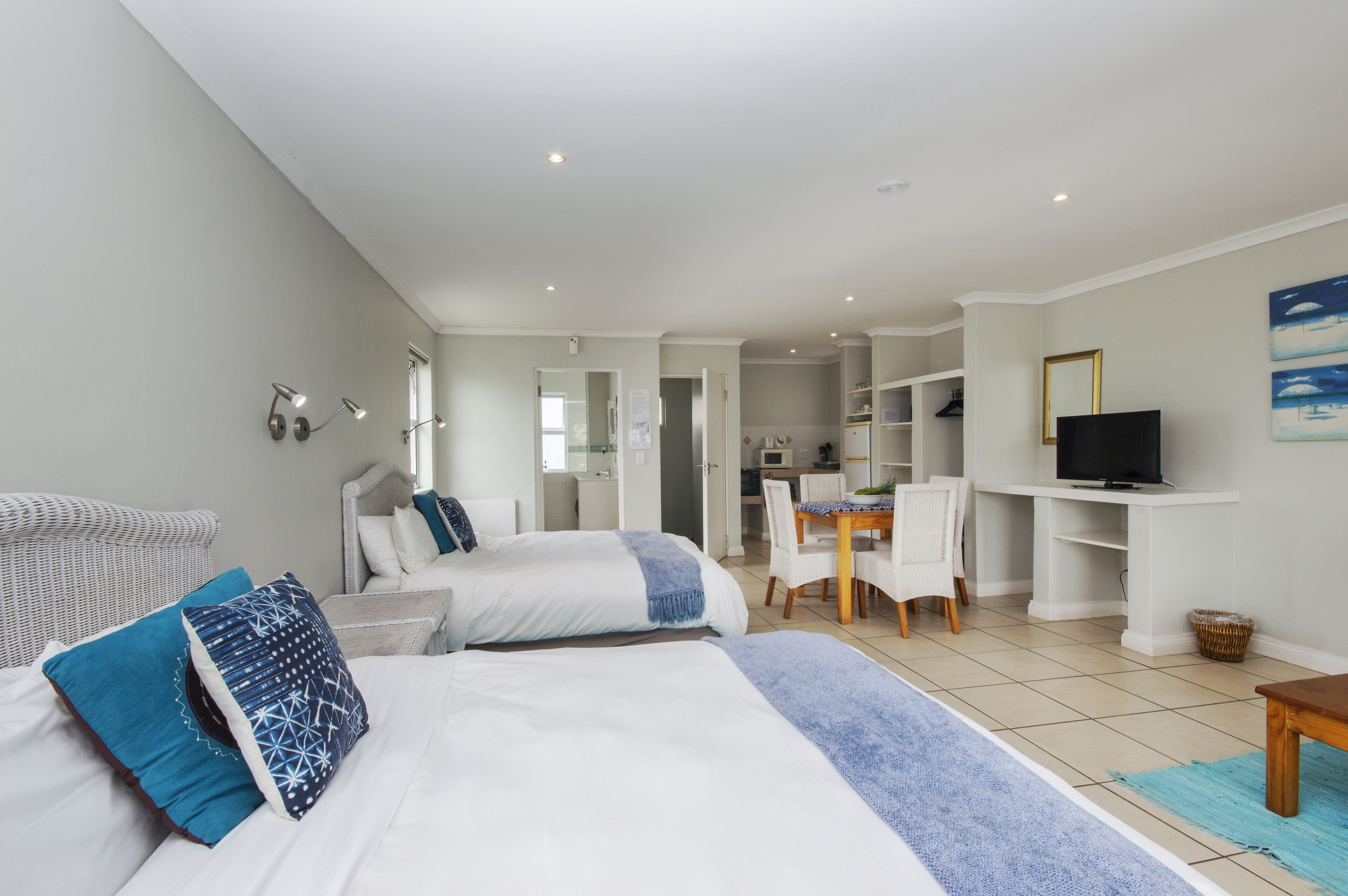 A hotel room with two beds, a dining area, a TV, and a kitchenette.