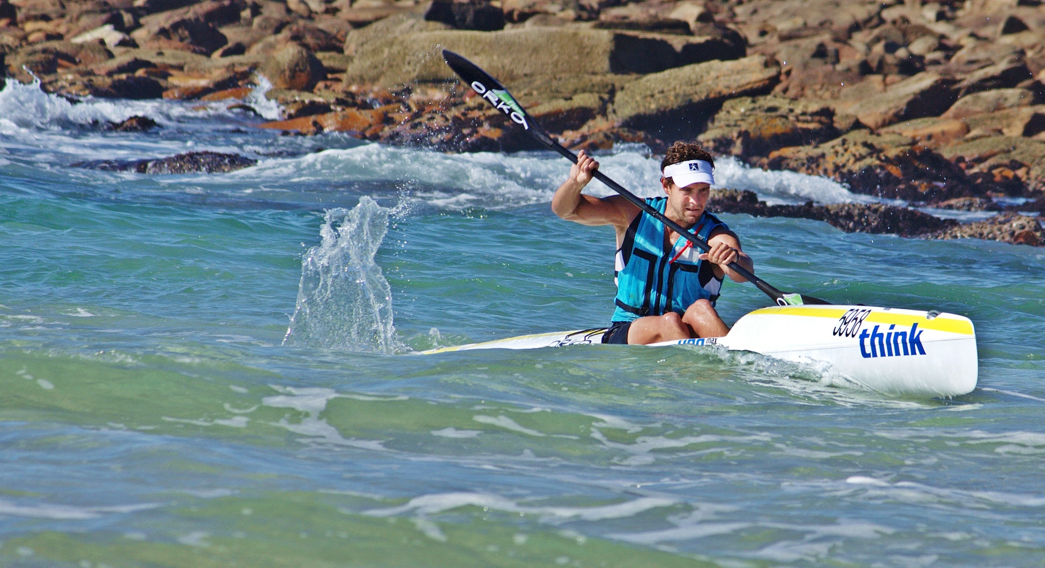 A person kayaking on a body of water with a kayak that has the word "think" on it.