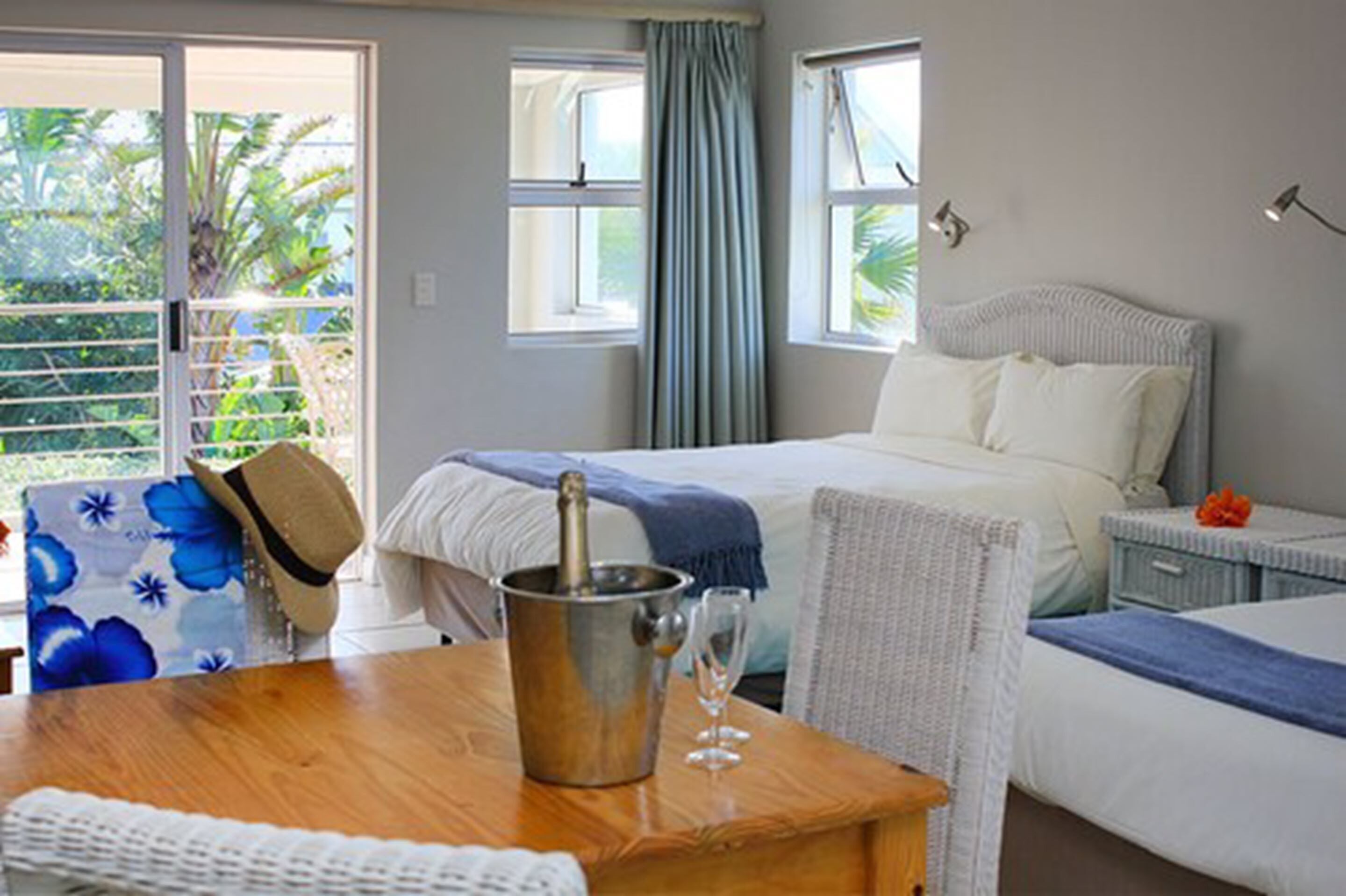 Habitación de hotel con cama, una mesita de noche con una botella de champán y copa, una silla y vistas al verde exterior.