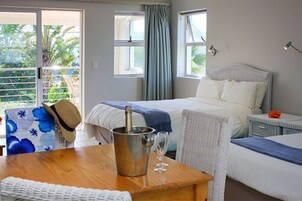 A hotel room with a bed, a bedside table with a champagne bottle and glass, a chair, and a view of greenery outside.