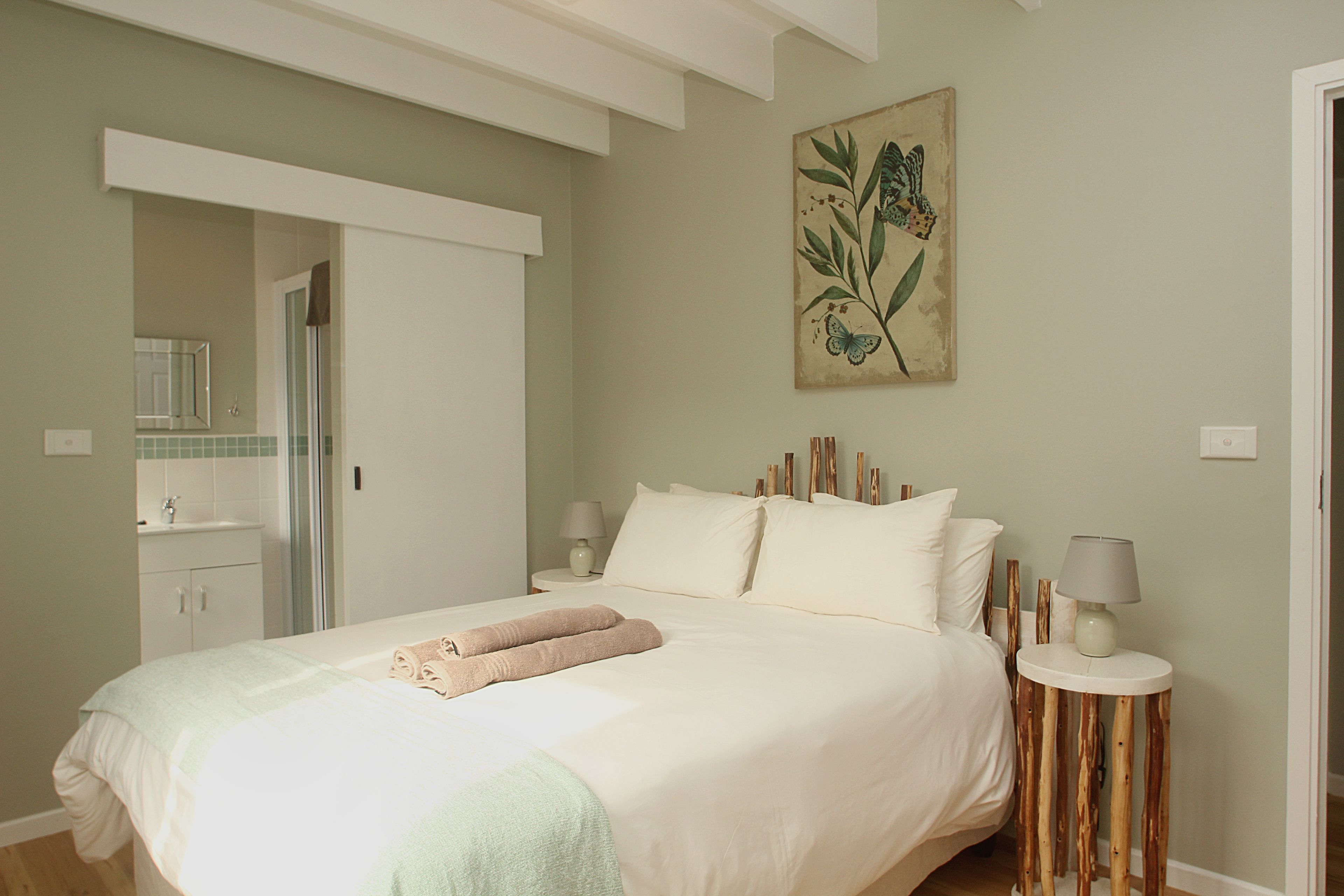 A bedroom with a bed, bedside tables, a mirror, and a painting on the wall.