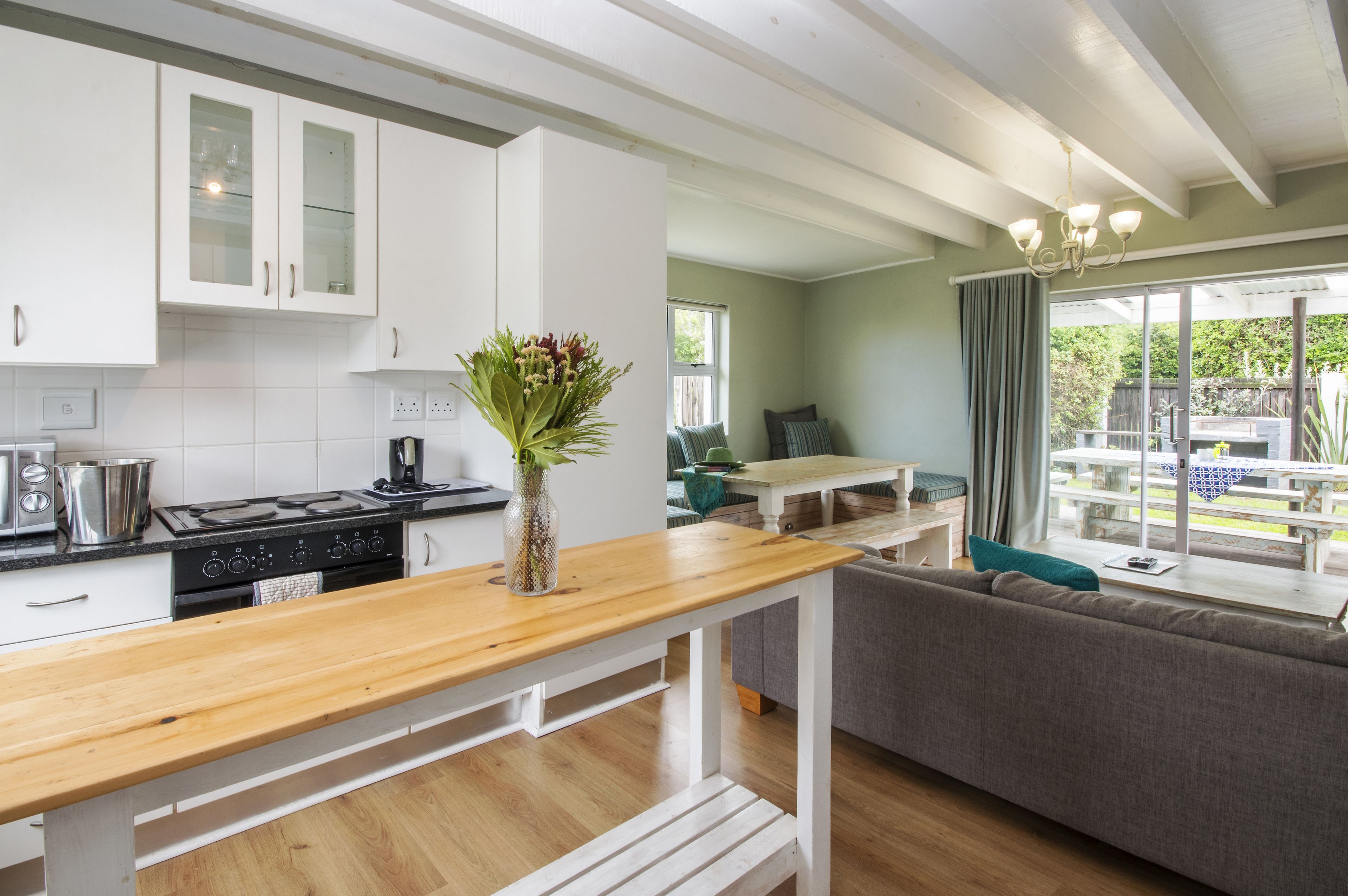 A modern kitchen with white cabinets, a wooden countertop, and a dining area with a bench and sofa.
