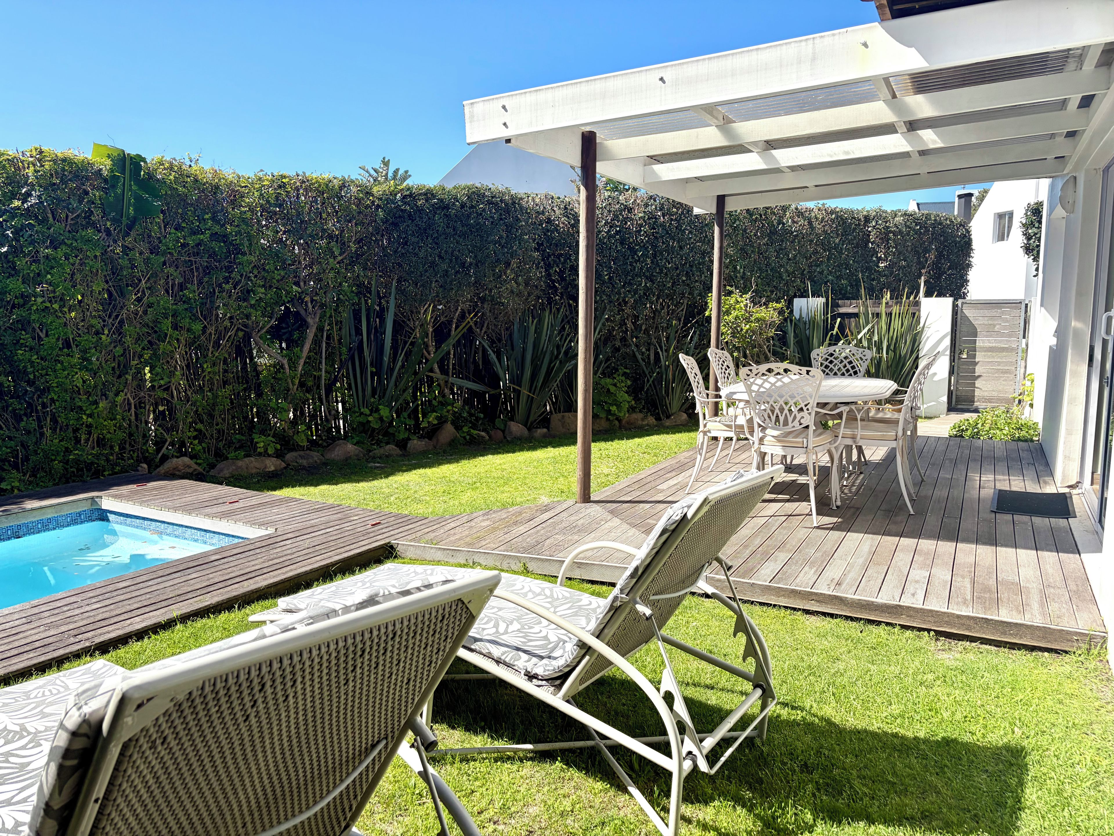 A backyard with a pool, a covered patio area, and outdoor furniture.