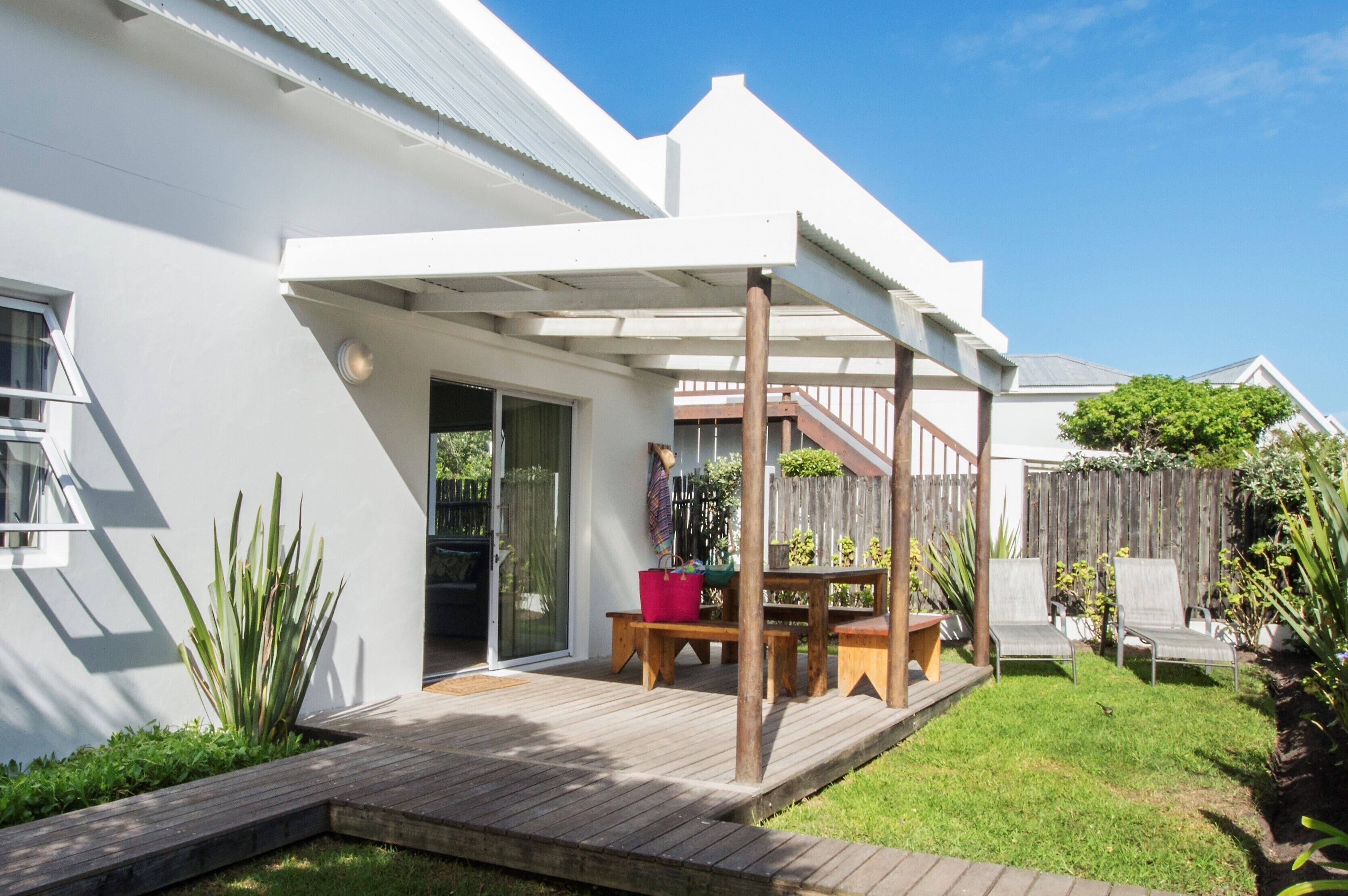 A modern house with a covered patio, a wooden deck, and a fenced backyard.