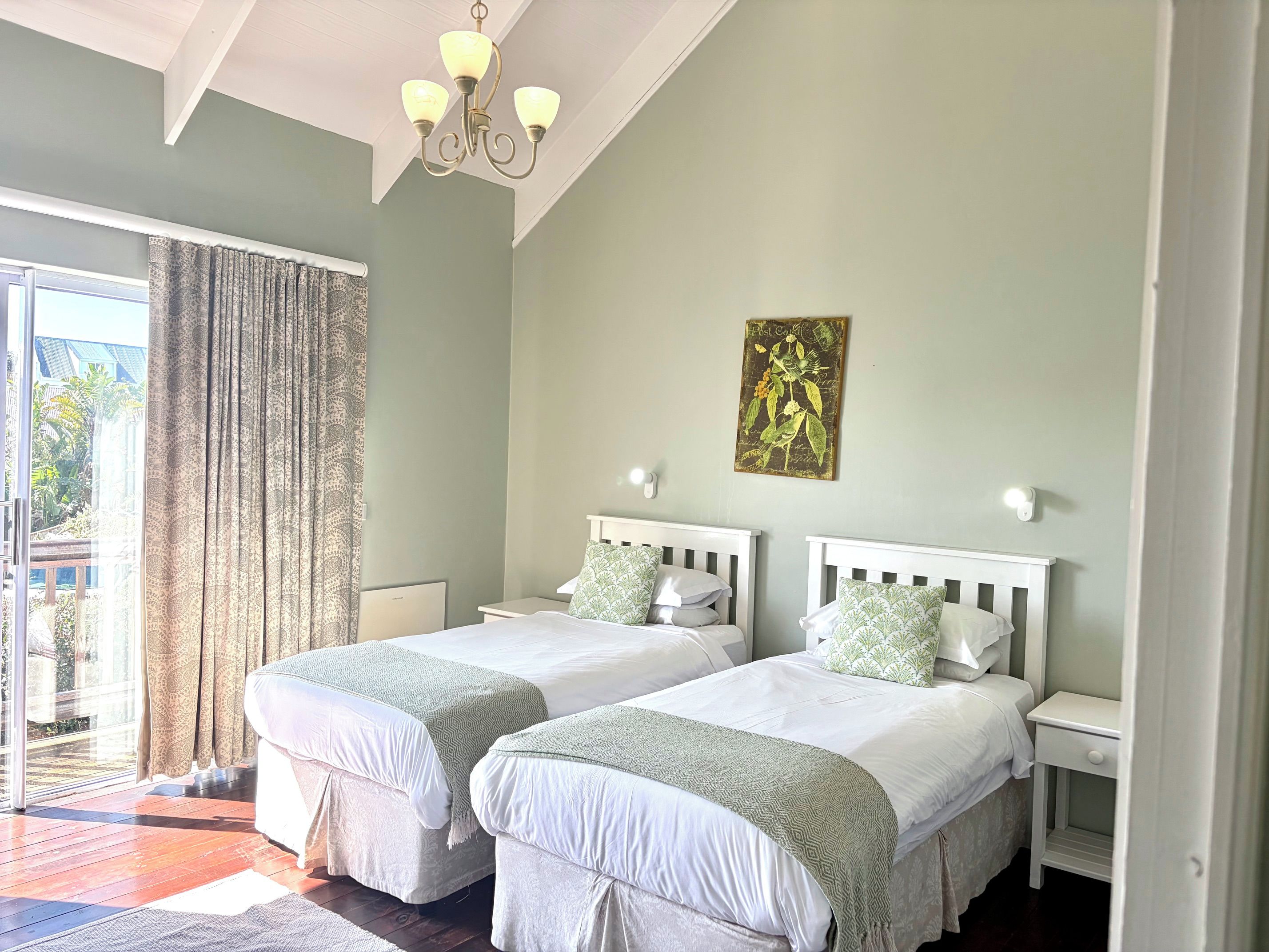 Une chambre avec deux lits, un lustre, une œuvre d’art accrochée au mur et une vue par une fenêtre avec des rideaux.
