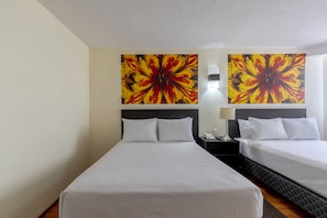 Habitación de hotel con dos camas, una mesita de noche con lámpara, y dos cuadros grandes con motivos florales en la pared.