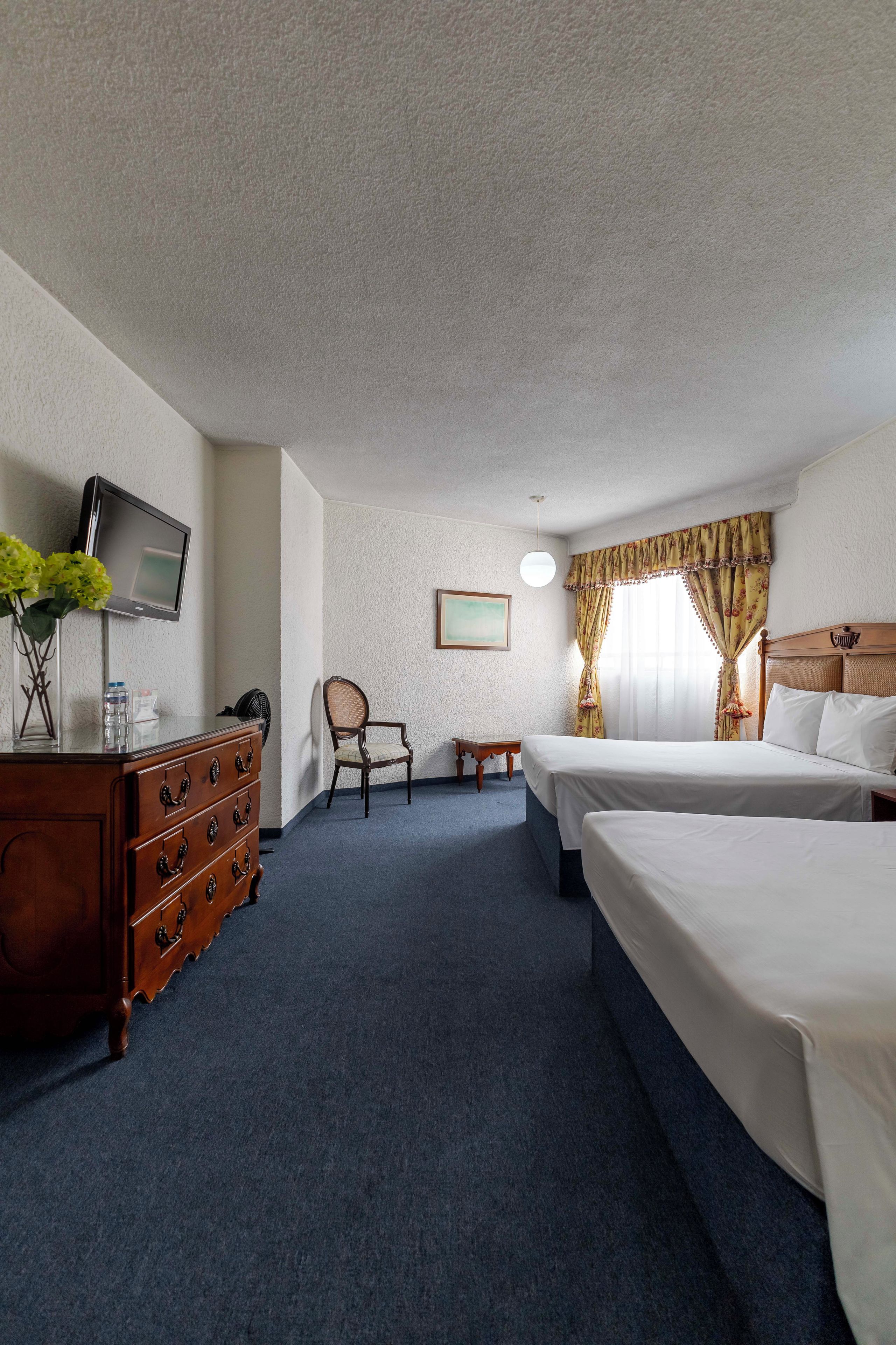 A hotel room with a wooden dresser, a television, a chair, two beds, and a small table.