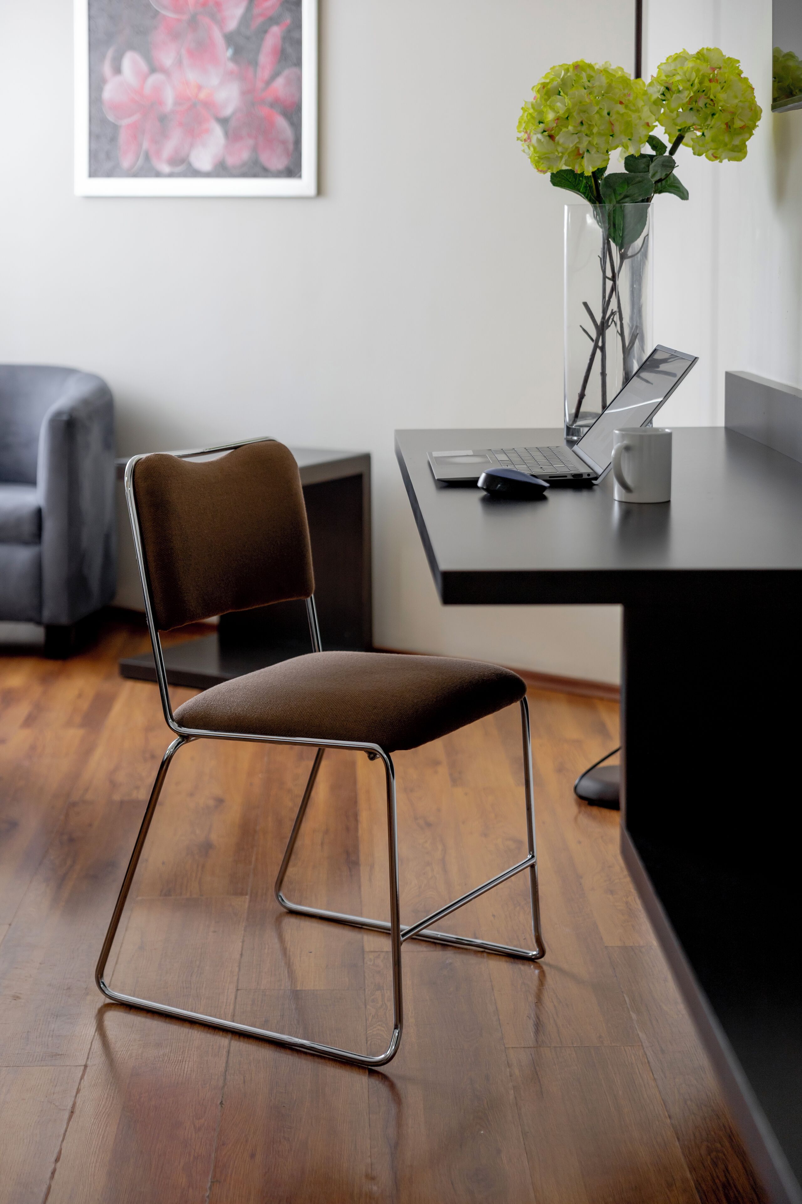 Una silla de oficina moderna con estructura metálica y asiento acolchado, sobre piso de madera.