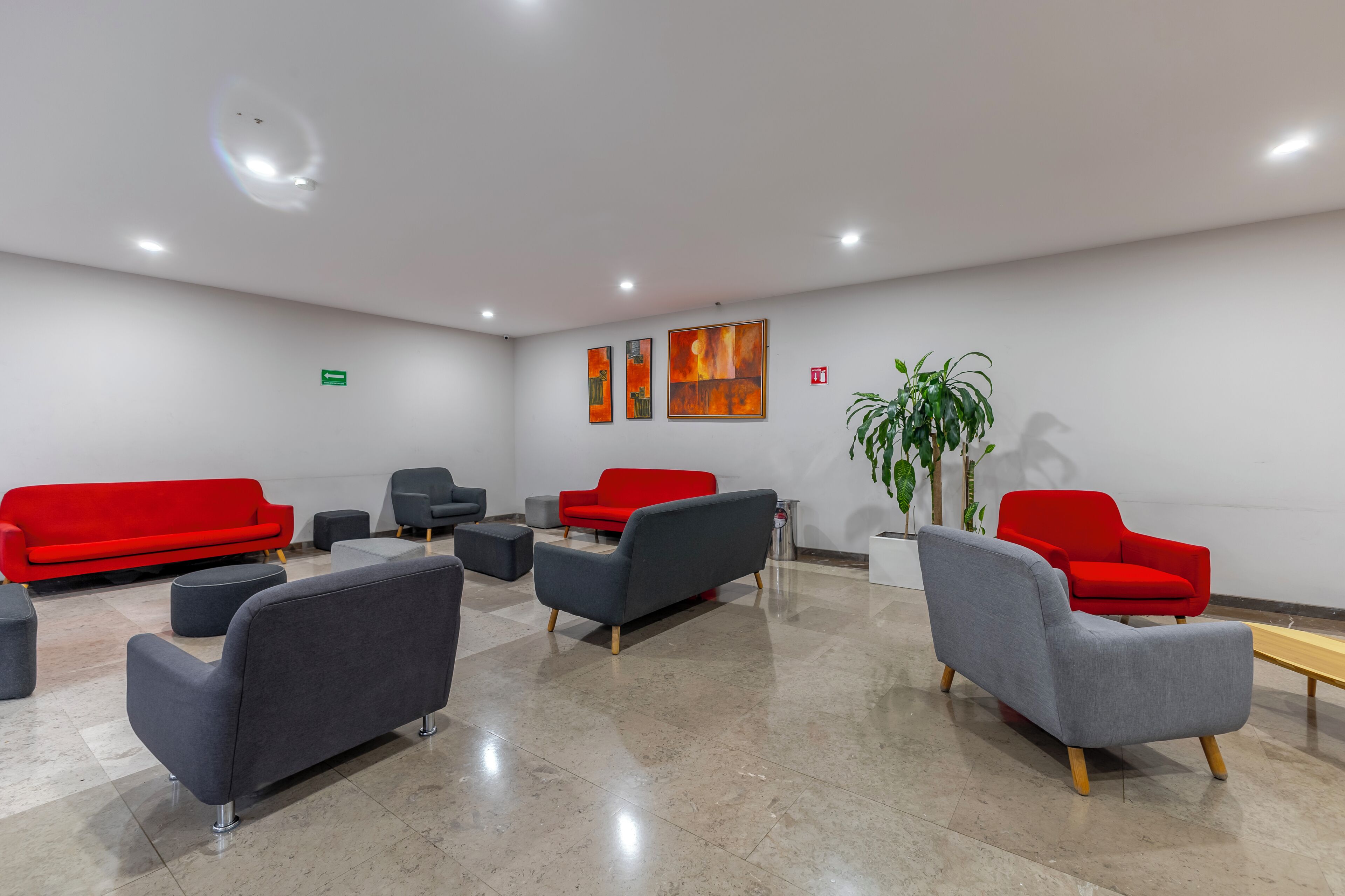 Un área de espera moderna con sofás rojos y grises, una mesa de centro y una planta en maceta.