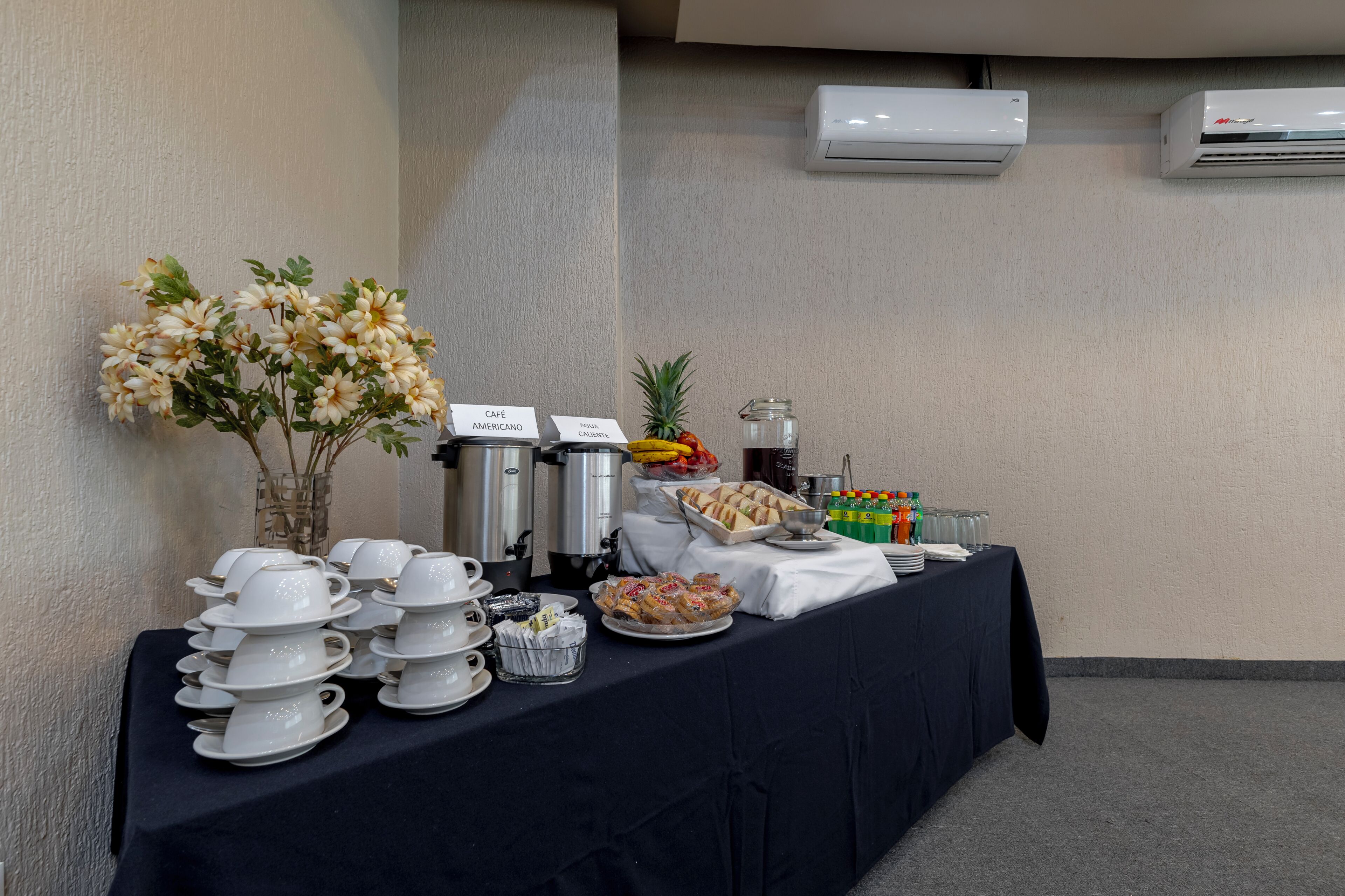 A buffet setup with coffee and tea stations, a fruit bowl, and a water dispenser.