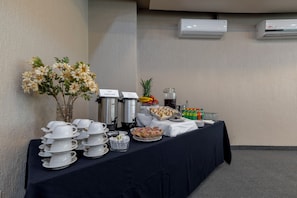 Montaje tipo buffet con estaciones de café y té, un bol de fruta y un dispensador de agua.
