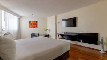A hotel room with a bed, a desk, a chair, a TV, and a window with curtains.