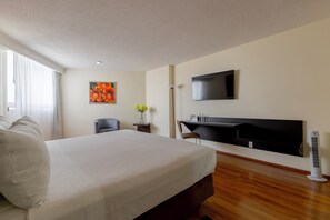 Una habitación de hotel con cama, escritorio, silla, televisor y ventana con cortinas.