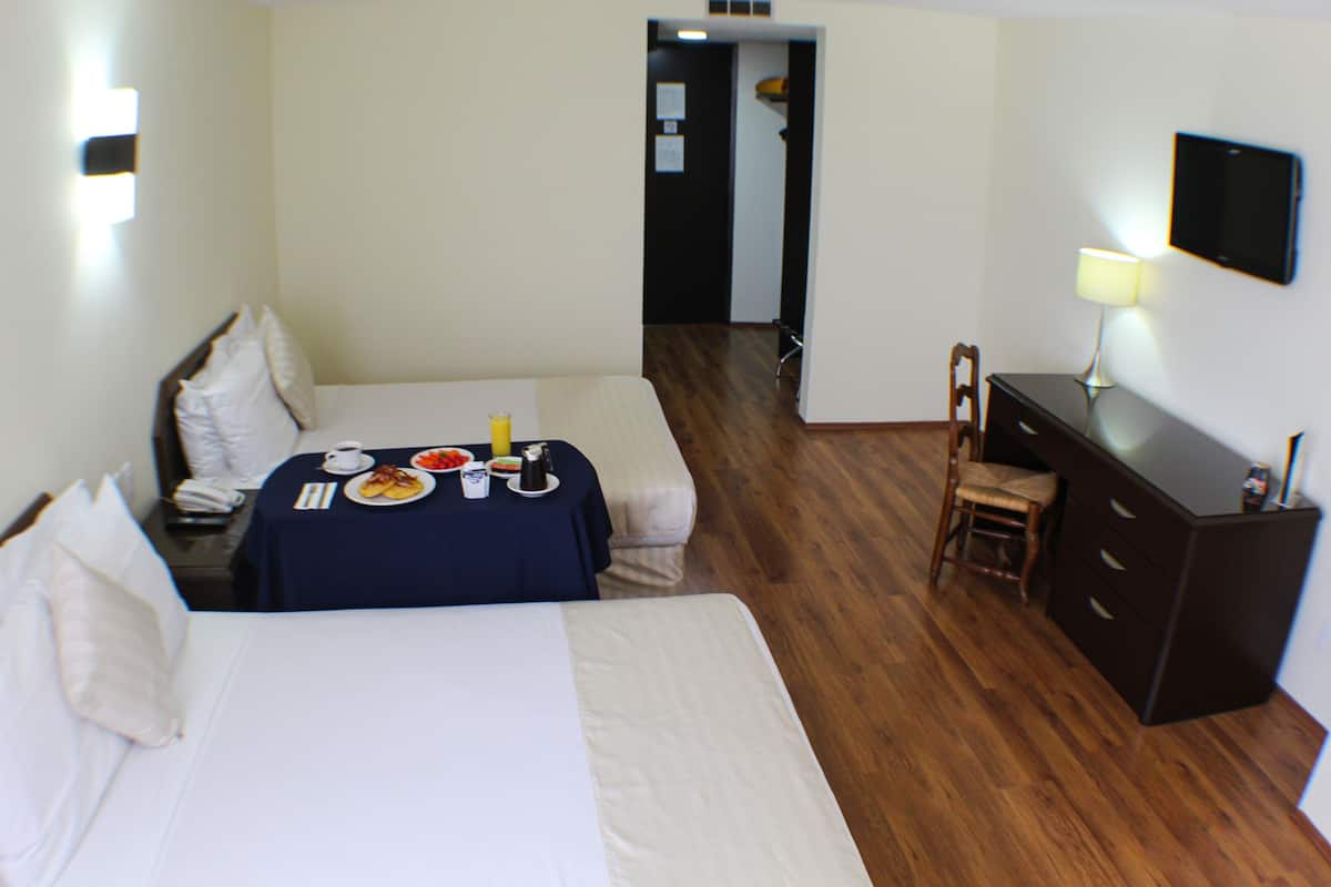 A hotel room with two beds, a desk with breakfast items, a chair, a TV, and a wooden floor.