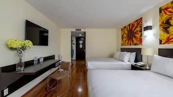 Habitación de hotel con televisión de pantalla plana, un florero con flores, un escritorio con silla y dos camas con ropa blanca.