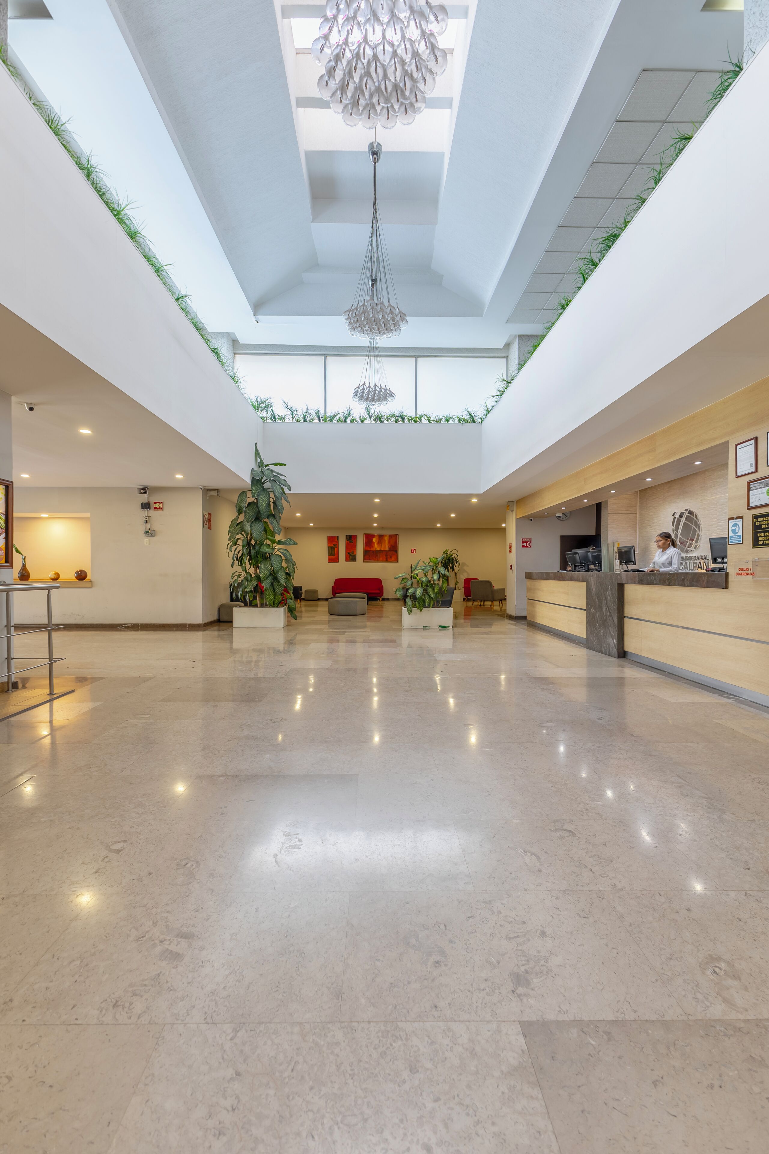 Eine geräumige Lobby mit hoher Decke, einem Empfangsschalter und einem modernen Kronleuchter.