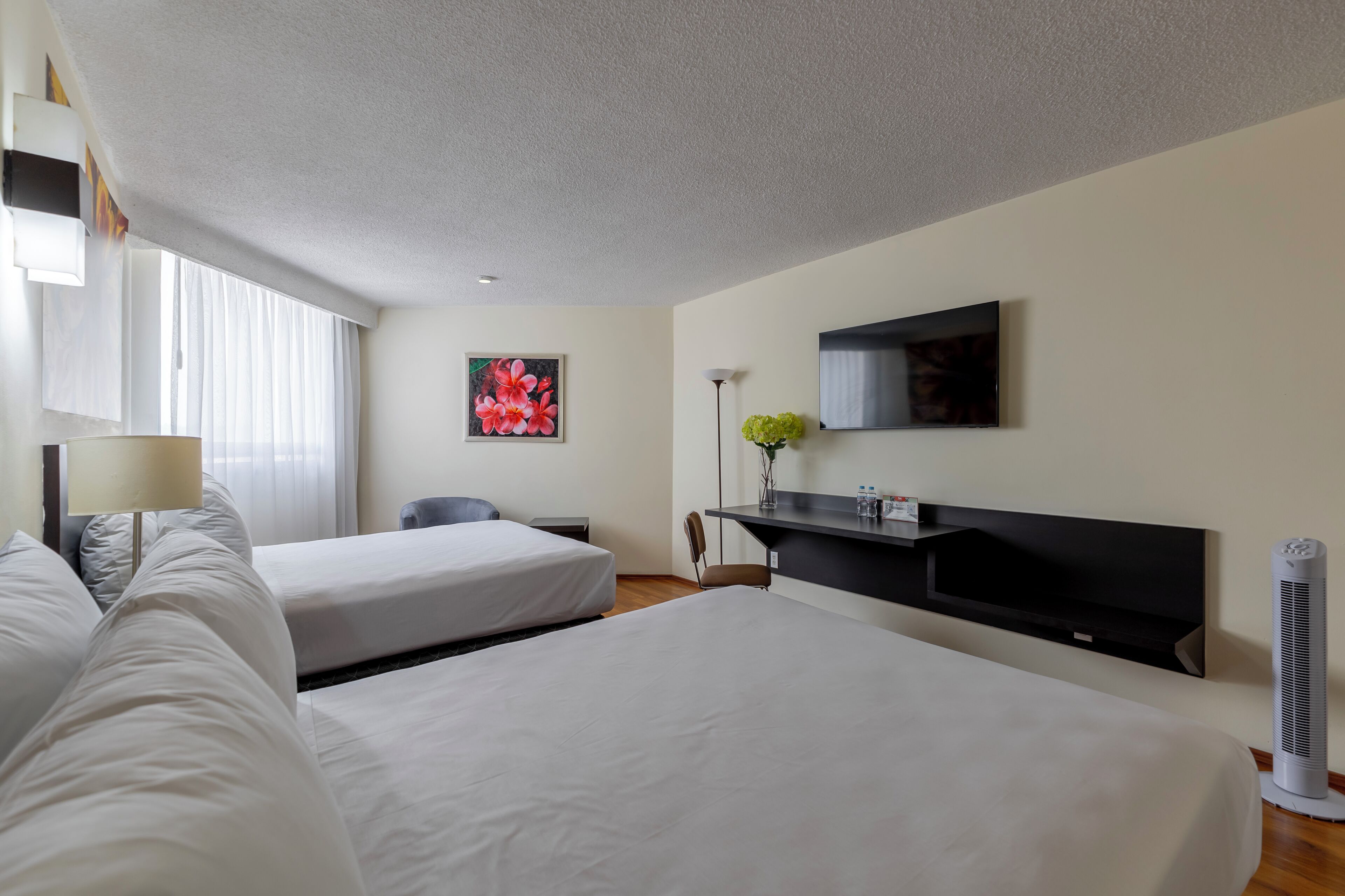 Una habitación de hotel con dos camas, un escritorio, una silla, un televisor y una ventana con cortinas.