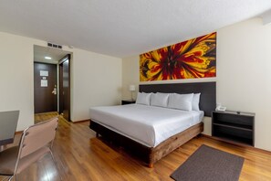 Habitación de hotel con una cama grande, una mesita de noche, un escritorio, una silla, un cuadro en la pared y suelo de madera.