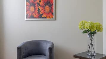 A room with a grey armchair, a vase with yellow flowers, and a painting of orange flowers on the wall.