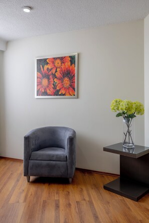 A room with a grey armchair, a vase with yellow flowers, and a painting of orange flowers on the wall. - Hotel Valle de Mexico Toreo (Naucalpan)
