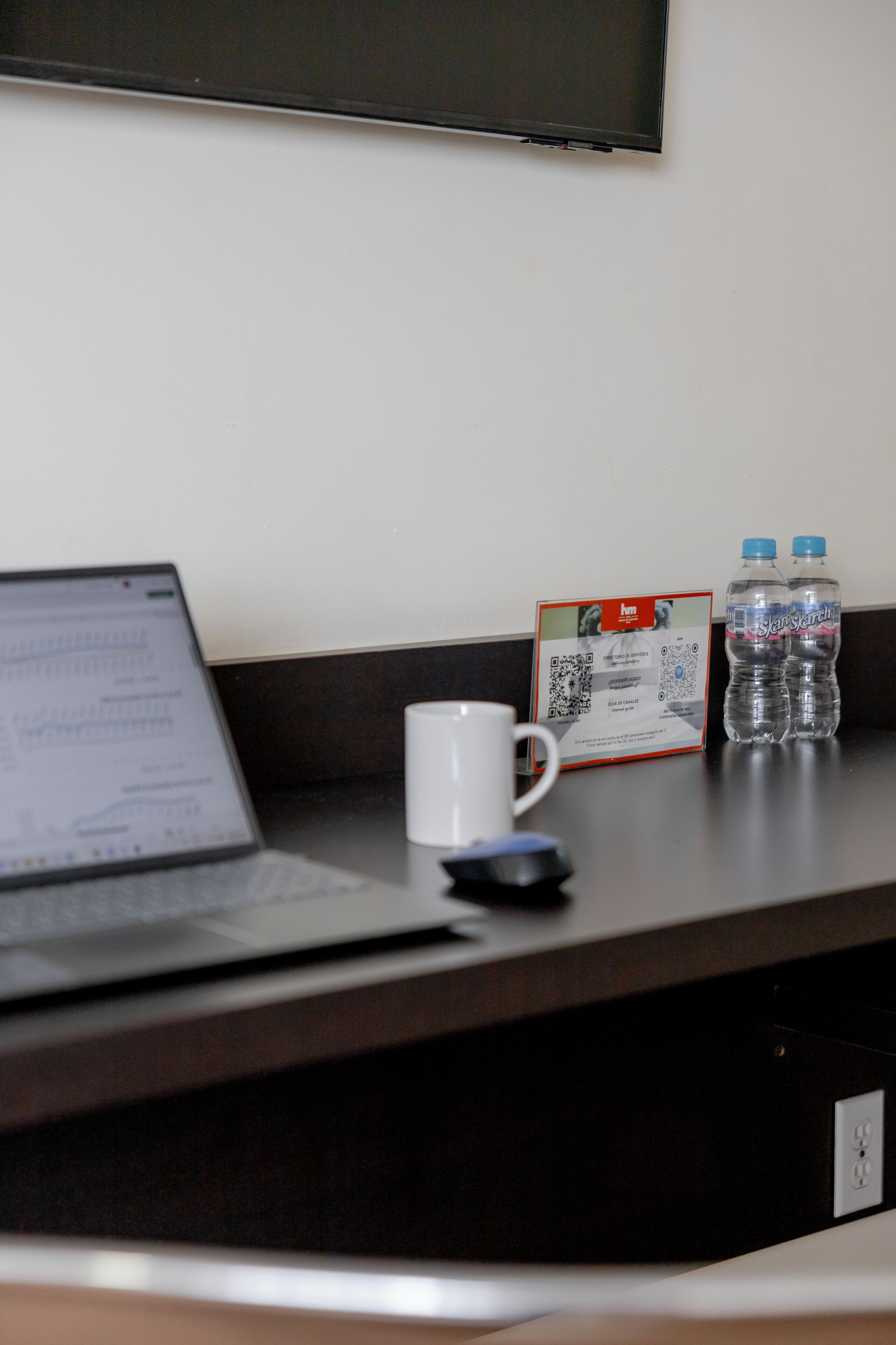Un escritorio con una computadora portátil, una taza blanca, una botella de agua y un documento impreso.