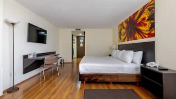 Una habitación de hotel con cama, mesita de noche, lámpara y un cuadro abstracto grande en la pared.