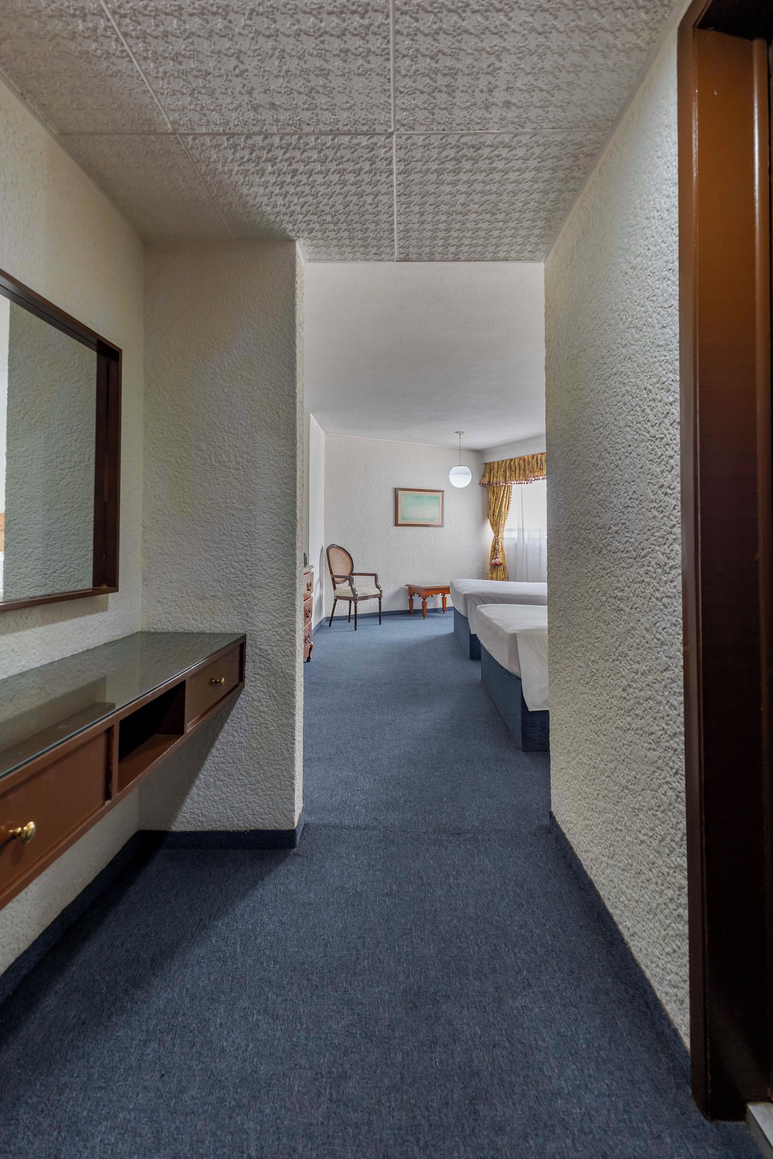 Ein Hotelzimmer mit einem großen Bett, einem Sessel, einem Schreibtisch und einem Spiegel.