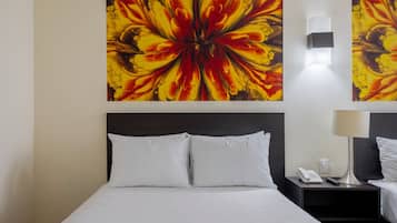 Hotelkamer met een bed, witte kussens, een nachtkastje met een lamp, een telefoon en een wandlamp.