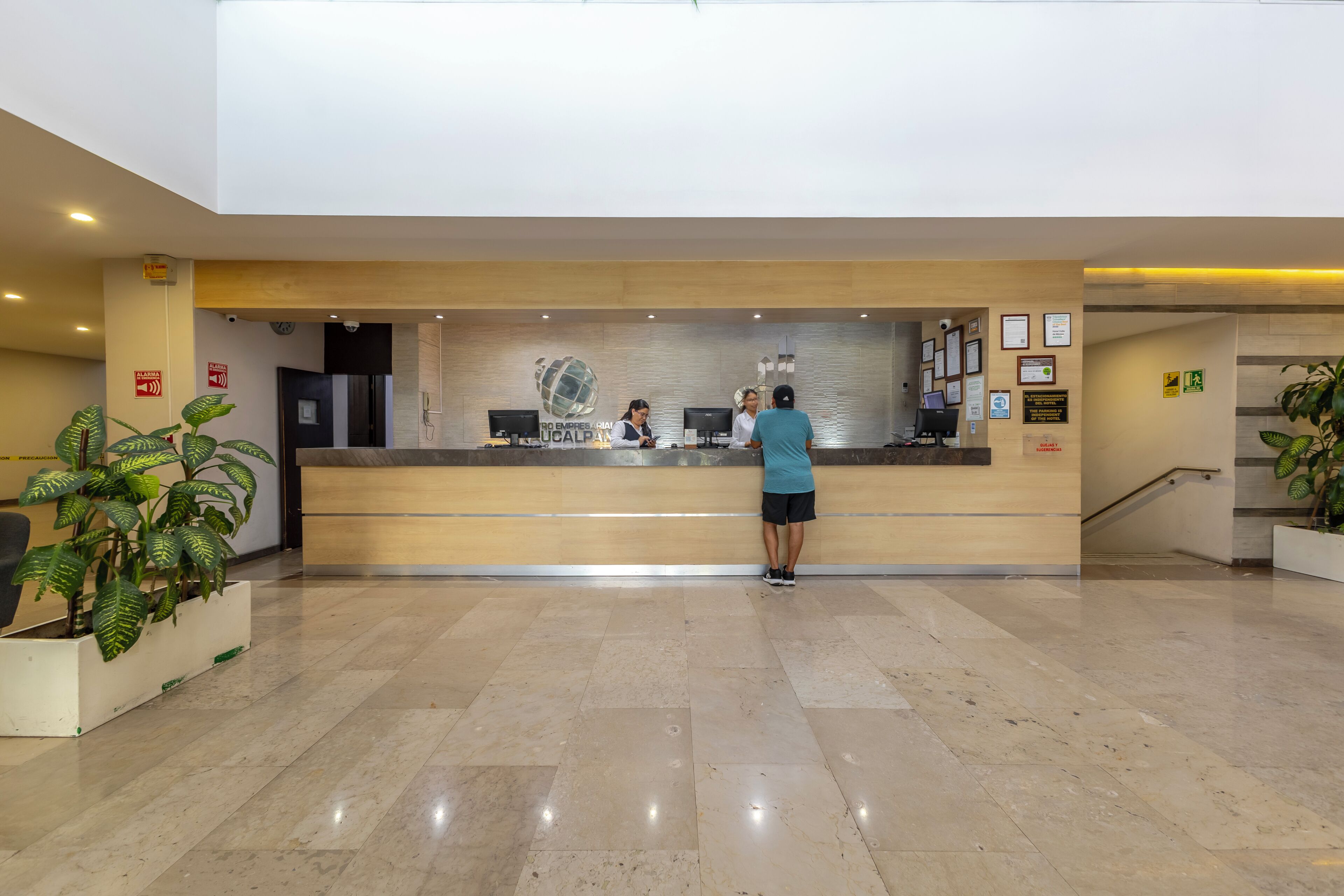Zona de recepción de hotel con mostrador, cámara de seguridad y un reloj en la pared.